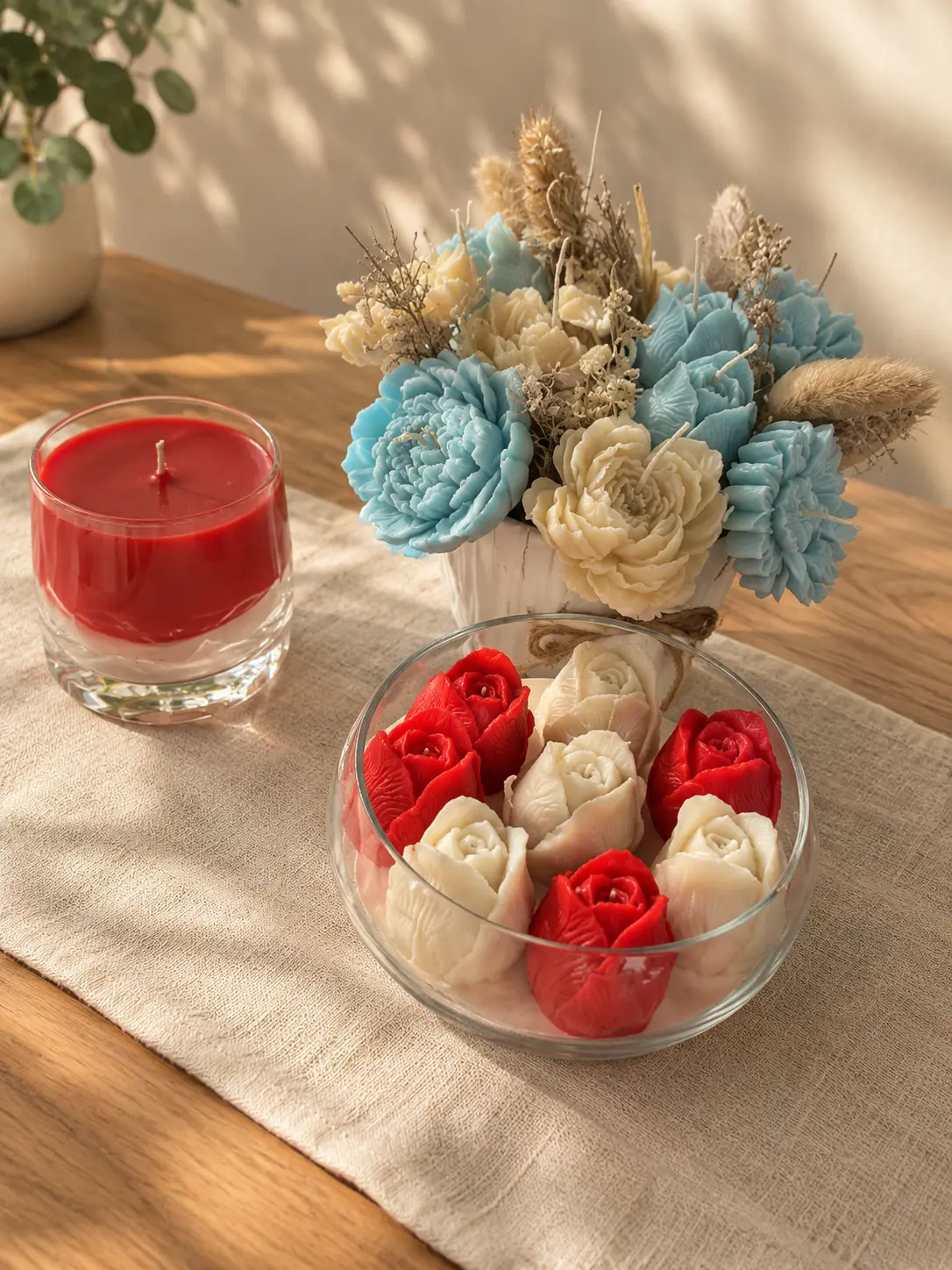 Arrangement of blue and cream wax flowers with rose candles in a glass bowl