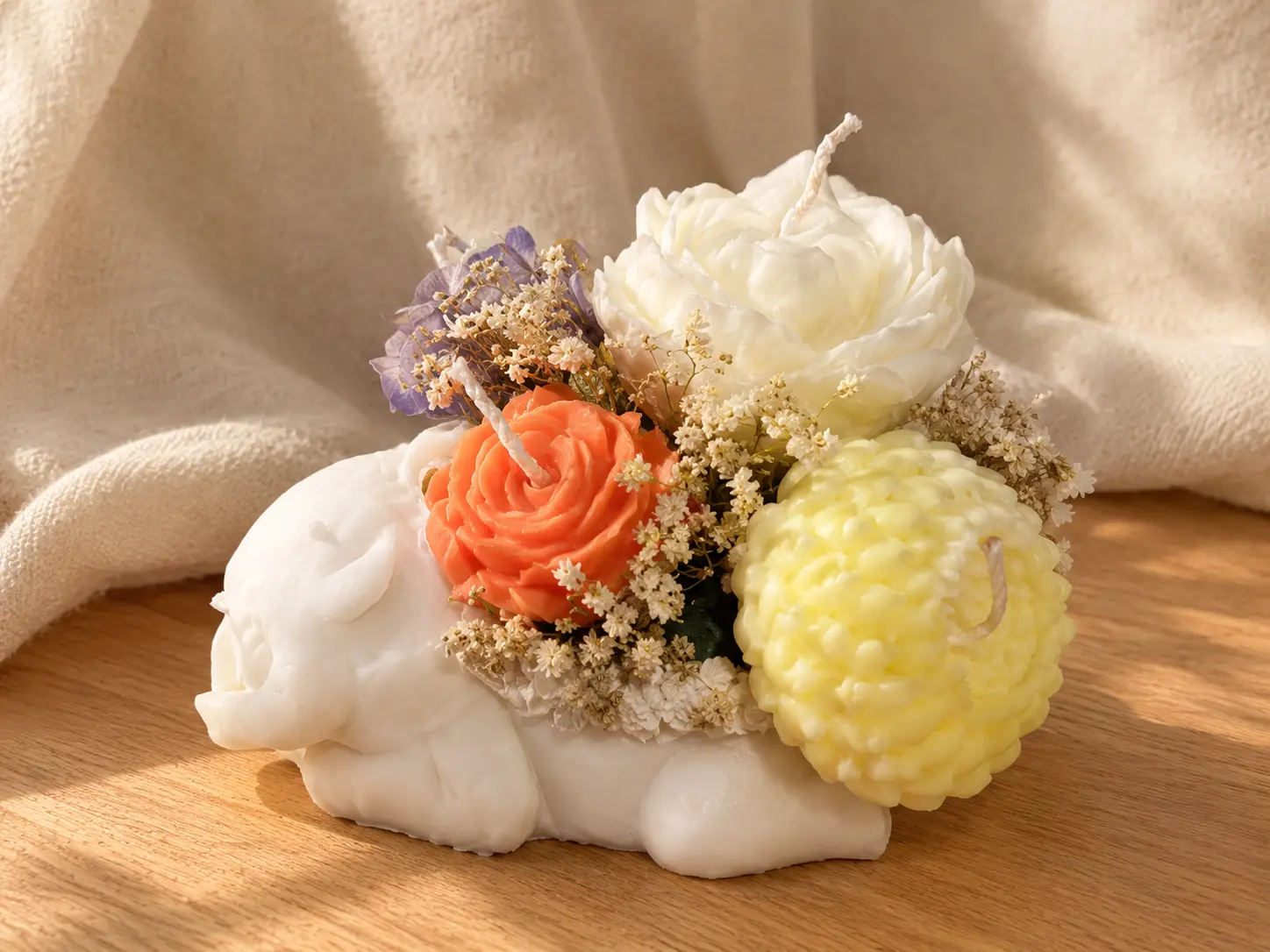 White lamb-shaped candle carrying orange, cream and yellow wax flowers