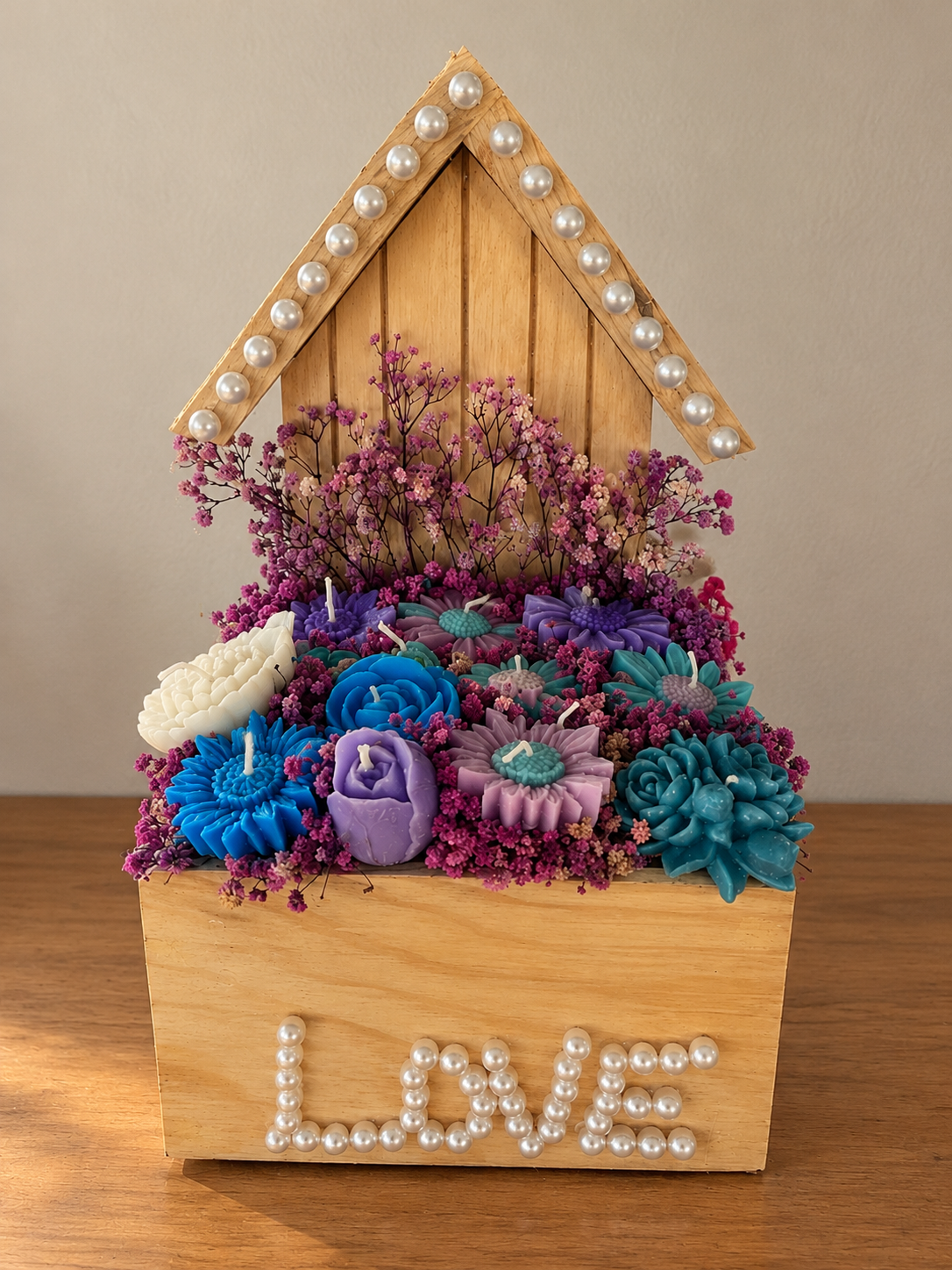 Wooden birdhouse box trimmed with pearls spelling LOVE, filled with blue, purple and white wax flower candles