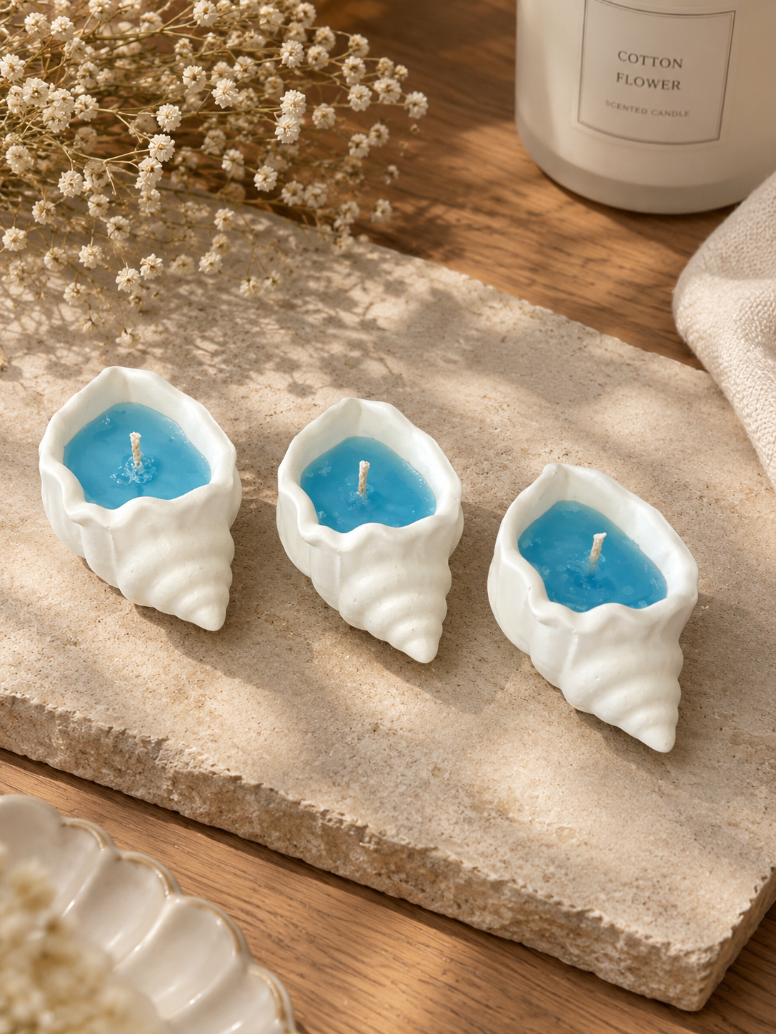 Three white seashell candles filled with blue wax on a stone tray