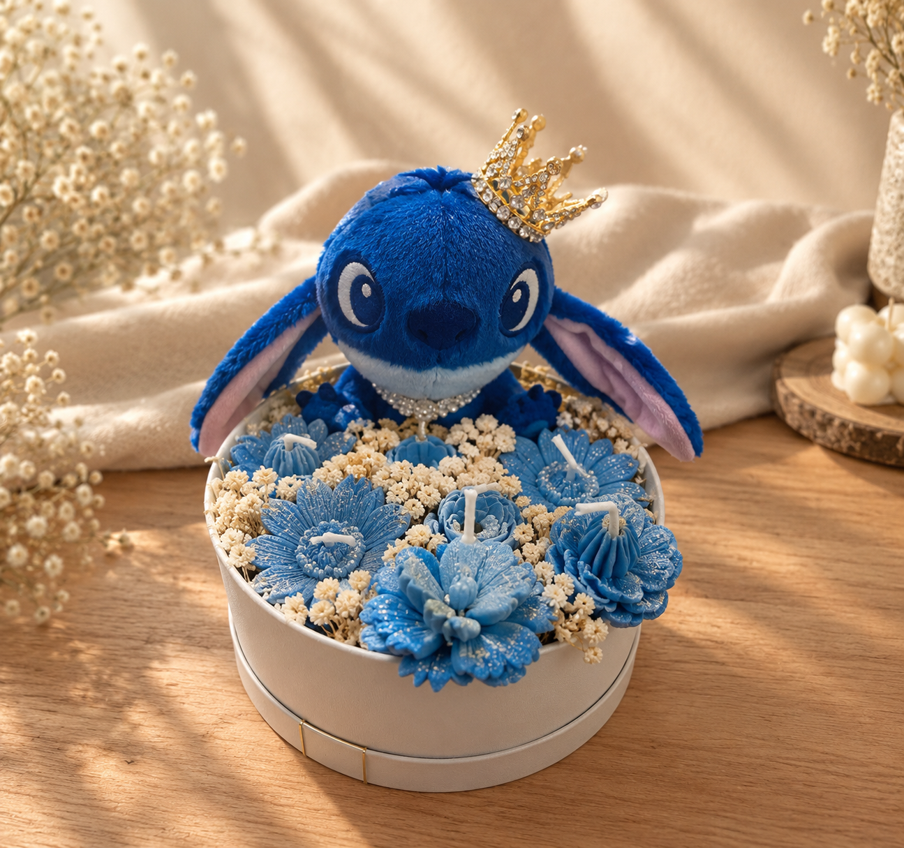 Round cream box of blue wax flower candles and cream dried flowers with a crowned blue plush character