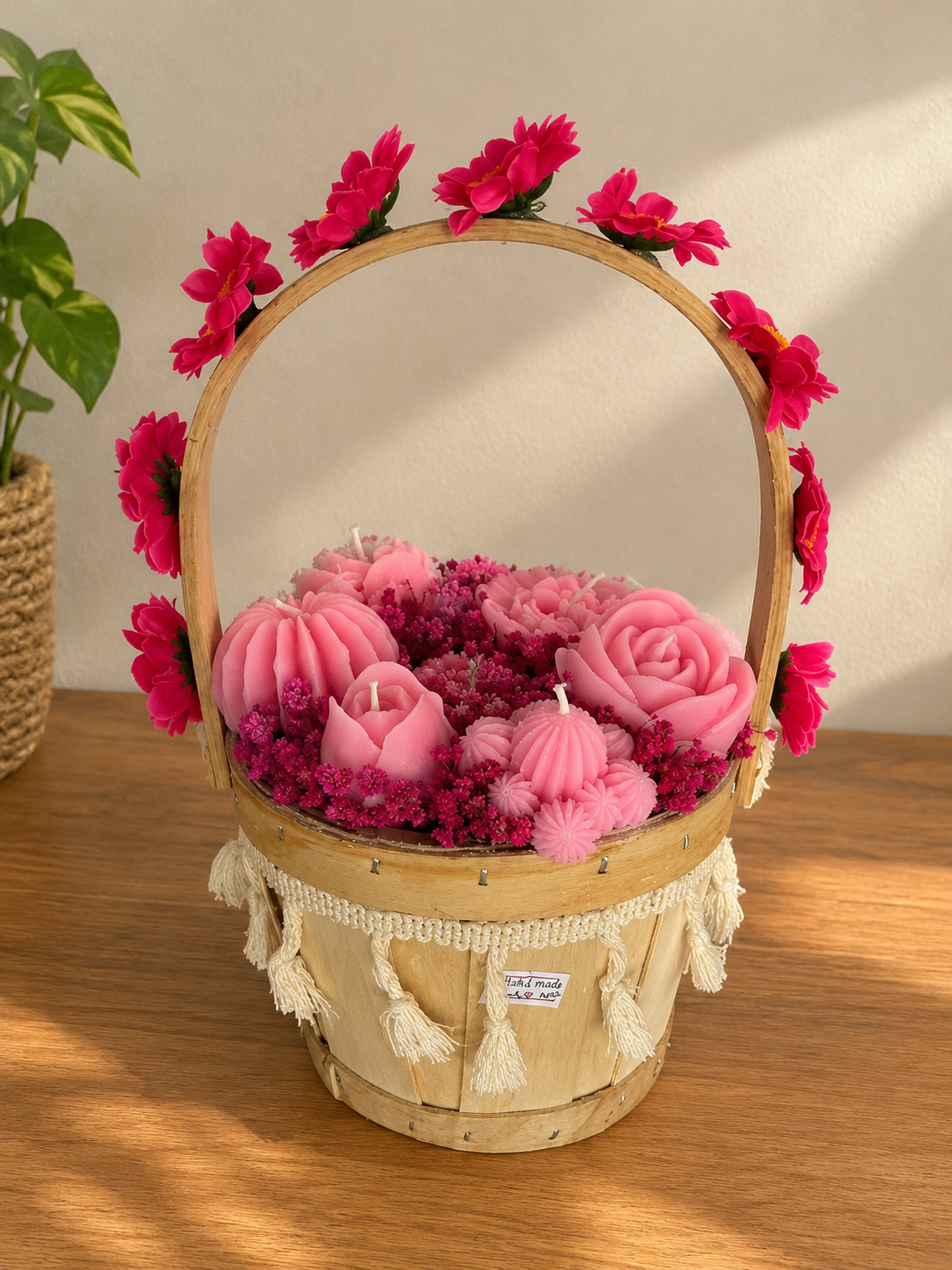 Wooden basket with tassels holding pink wax rose and flower candles, its handle lined with pink flowers