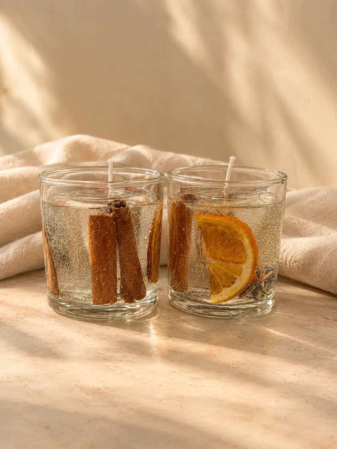 Two clear gel candles with cinnamon sticks and a dried orange slice