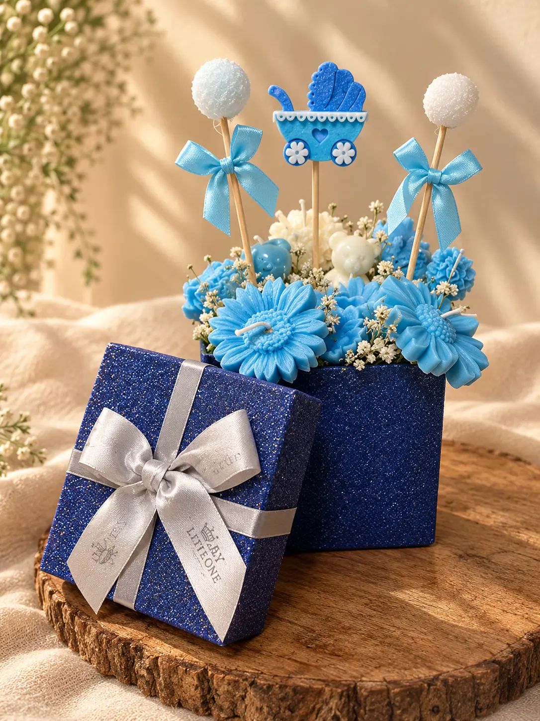 Blue glitter gift box filled with blue and white wax flowers, bears and a pram topper
